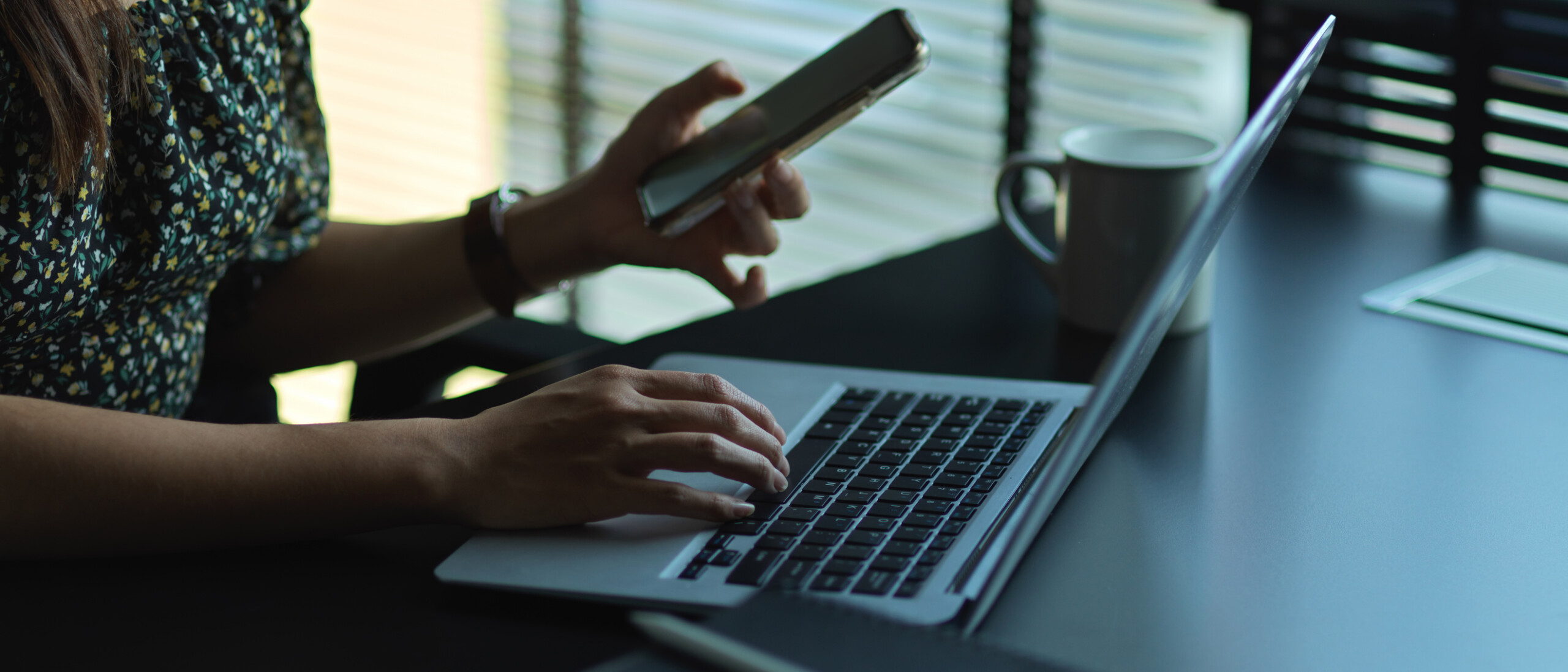 Closeup of a woman using a laptop and smartphone.