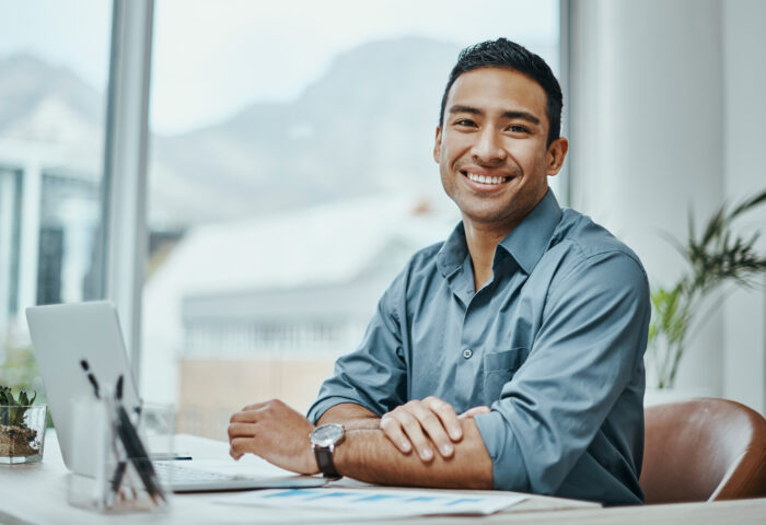 Young male professional sitting at a desk smiling at the camera.