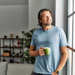 Smiling man drinking coffee and looking out the window.