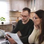 Young couple sitting at kitchen table, reading documents and calculating bills